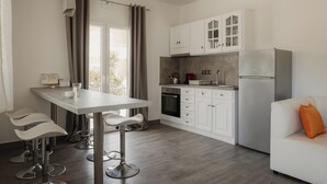 A modern kitchen with white cabinets, a stainless steel refrigerator, and a dining area with bar stools. - Mariu Canal d'Amour (Peroulades)