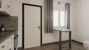 Una cucina moderna con un bollitore, una porta bianca, una finestra con tende e un piccolo tavolo.