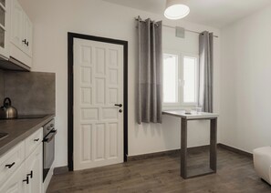 Eine moderne Küche mit Wasserkocher, einer weißen Tür, einem Fenster mit Vorhängen und einem kleinen Tisch.