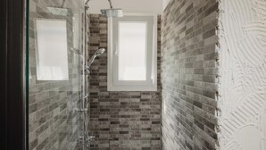 A bathroom with a shower, a window, and a brick wall. - Mariu Canal d'Amour (Peroulades)