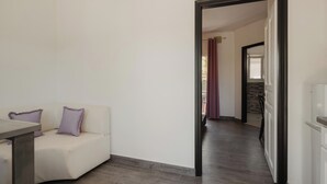 A modern living room with a sofa, a dining table, and a hallway leading to another room. - Mariu Canal d'Amour (Peroulades)