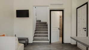 Un interno moderno con una scala, una TV a schermo piatto, una porta bianca e una panca.