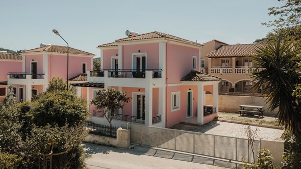 A pink building with a balcony, a fence, and a palm tree. - Mariu Canal d'Amour (Peroulades)