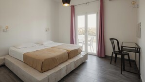 Una stanza con due letti, un tavolo, una sedia, una lampada a sospensione e una porta scorrevole in vetro che dà su uno spazio esterno.