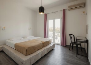 Ein Zimmer mit zwei Betten, einem Tisch, einem Stuhl, einer Hängeleuchte und einer Schiebetür zu einem Außenbereich.