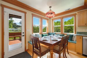 A dining area with a wooden table, chairs, and a bench. There are large windows with a view of greenery outside. - Hot tub, family and dog friendly, 1 1/2 block to beach, surrounded by nature (Nehalem)