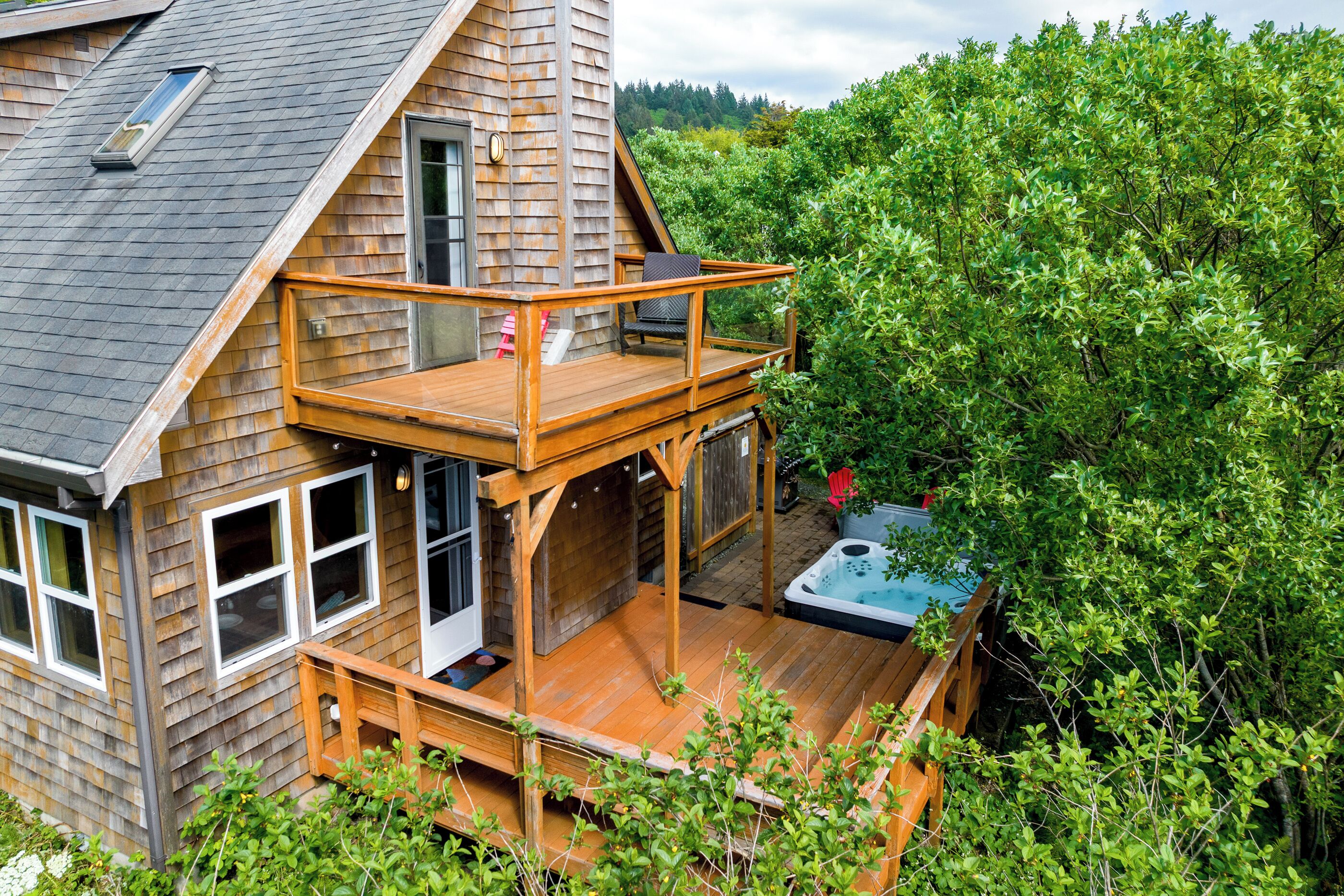 Una casa de madera con terraza, jacuzzi y vista a follaje denso.
