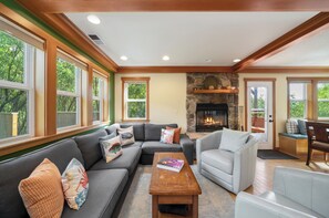 A living room with a sectional sofa, a fireplace, and large windows. - Hot tub, family and dog friendly, 1 1/2 block to beach, surrounded by nature (Nehalem)