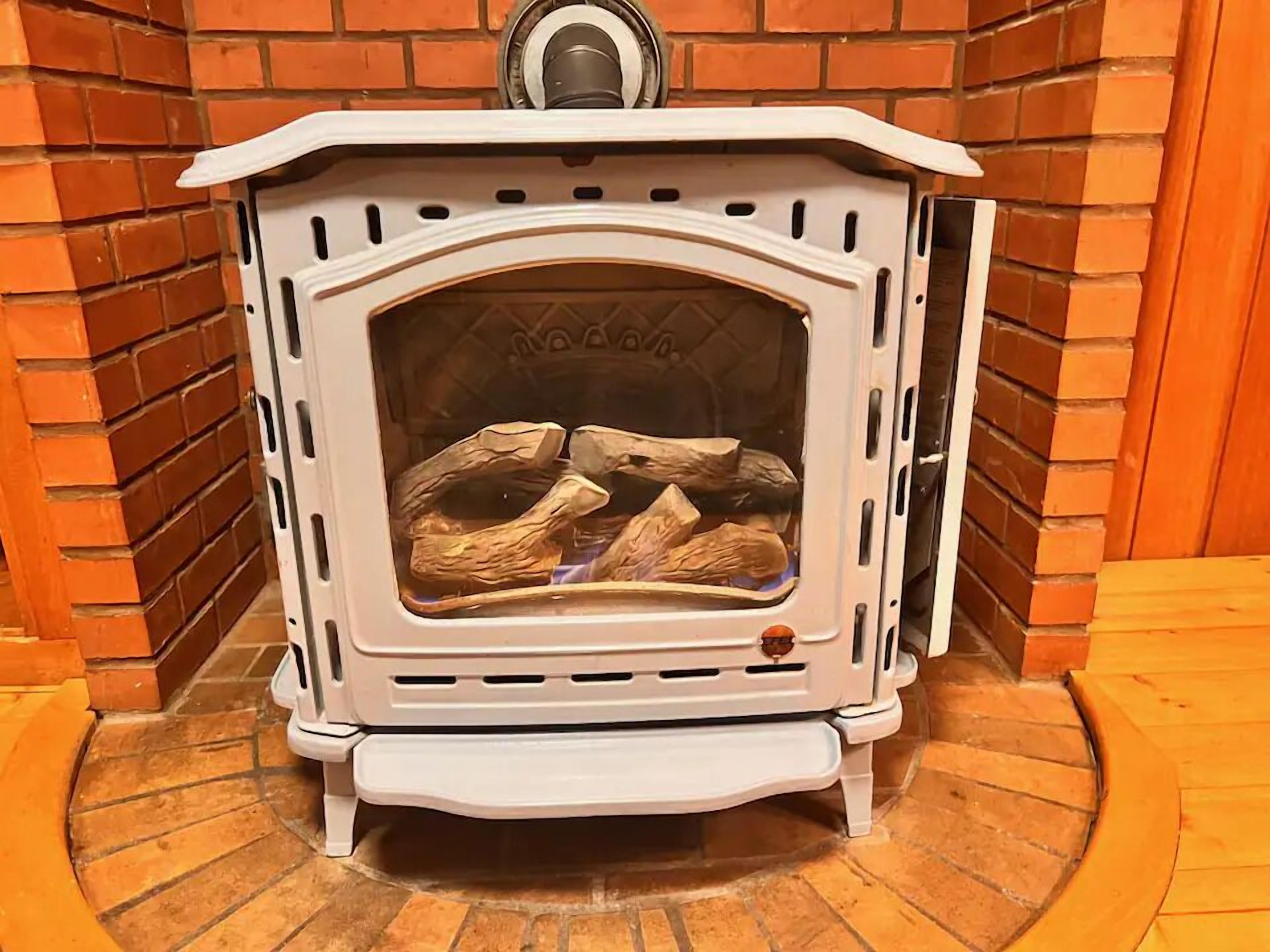 A white wood-burning stove with a glass door, set against a brick wall.