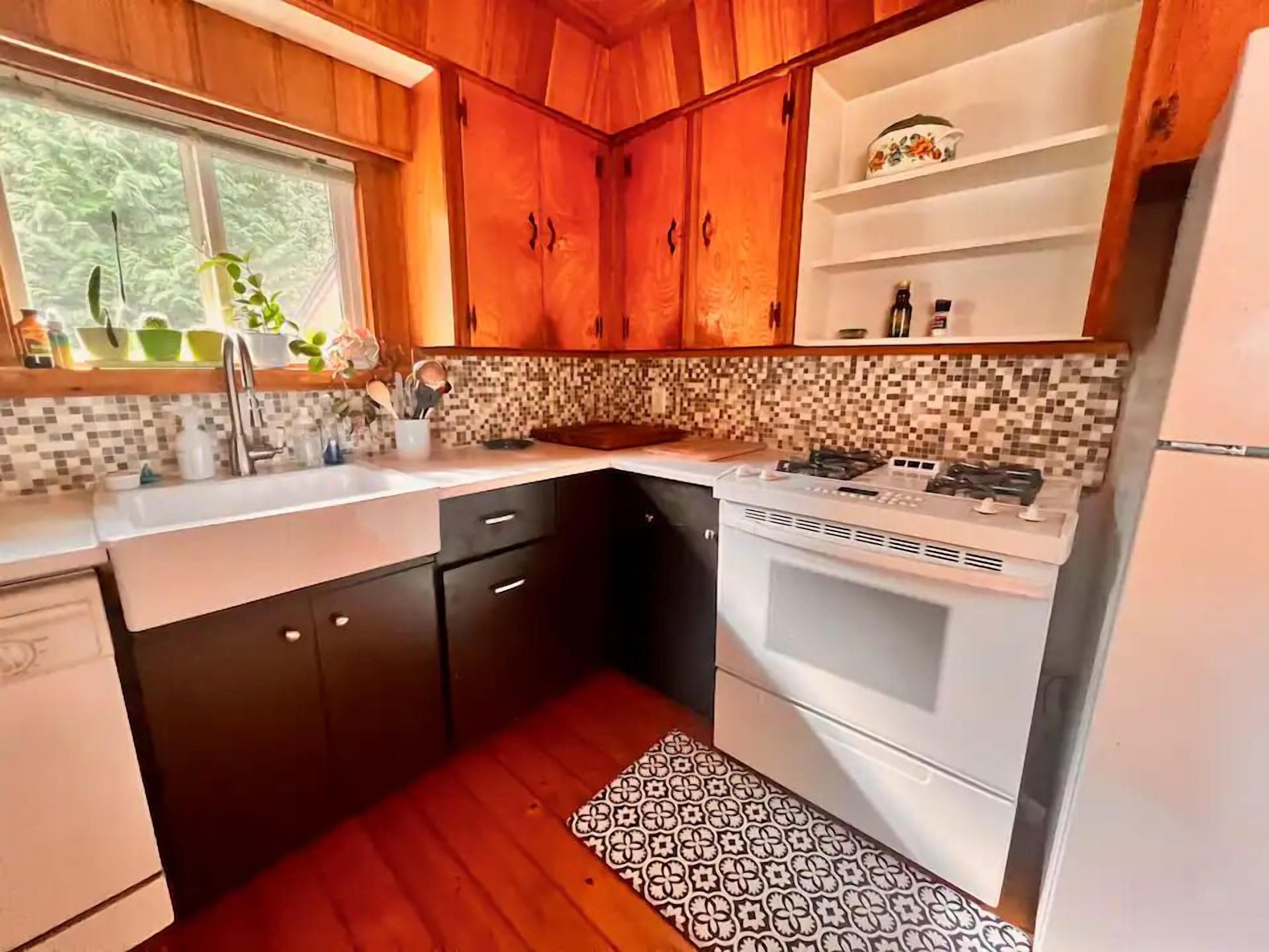 Una cocina con armarios de madera, salpicadero de azulejos, estufa a gas y un lavamanos.