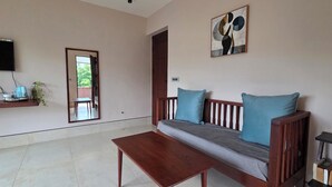 A living room with a sofa, a coffee table, a TV mounted on the wall, and a door leading outside. - Nirmala's Farm House (Courtallam)