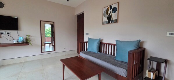 A living room with a sofa, a coffee table, a TV mounted on the wall, and a door leading to an outdoor area.