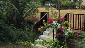 A garden with a staircase leading to a building, surrounded by greenery and mountains in the background. - Nirmala's Farm House (Courtallam)