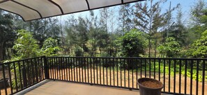 A balcony with a metal railing, a potted plant, and a view of a forested area. - Nirmala's Farm House (Courtallam)
