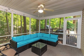 A covered porch with a sectional sofa, a glass coffee table, and a ceiling fan.