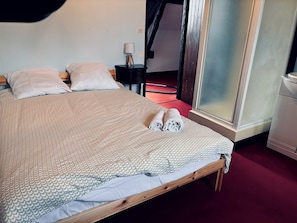 Ein ordentlich bezogenes Bett mit einem gemusterten Bettüberwurf, zwei Kissen und zwei aufgerollten Handtüchern.