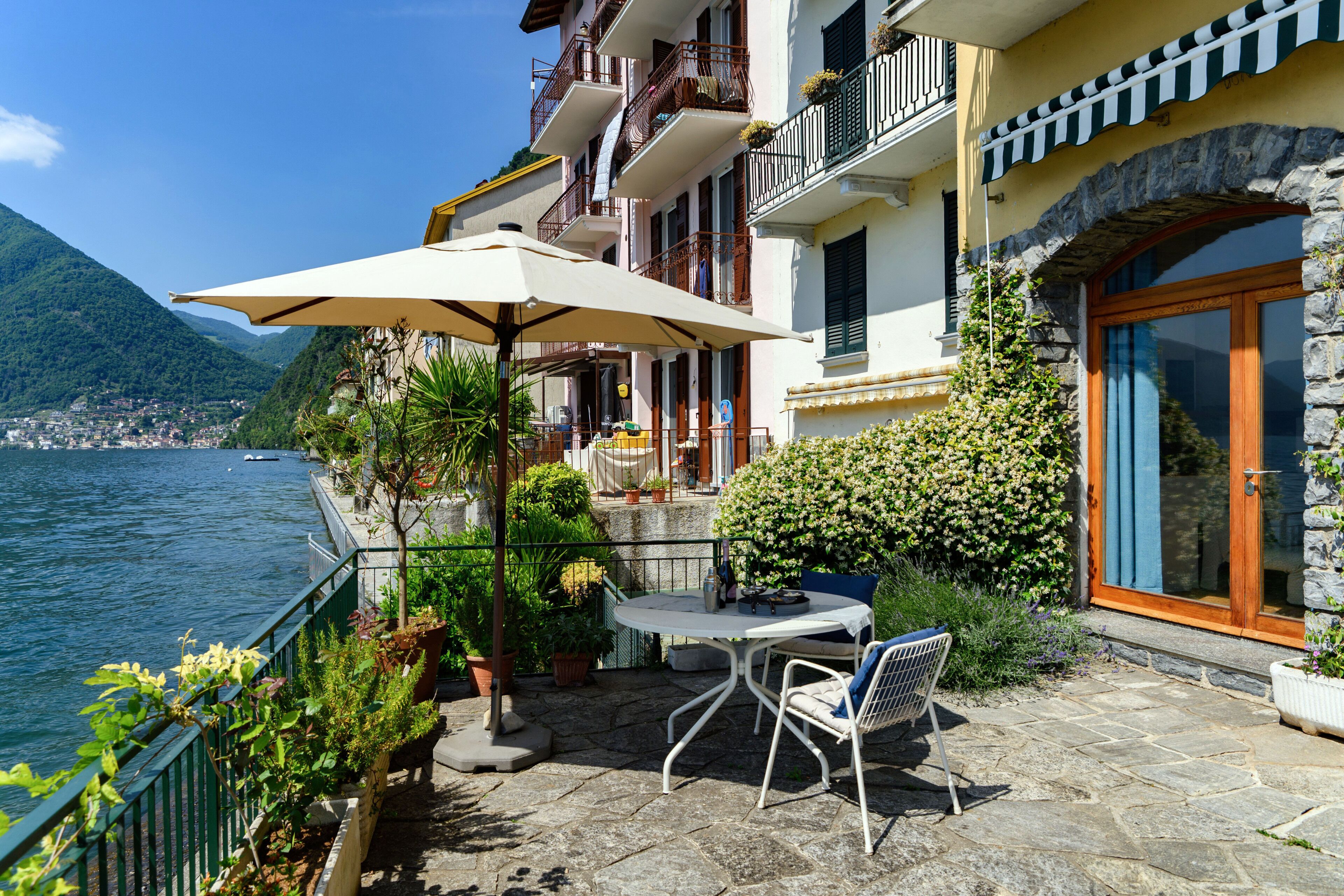 A terrace with a table and chairs, overlooking a body of water and mountains.