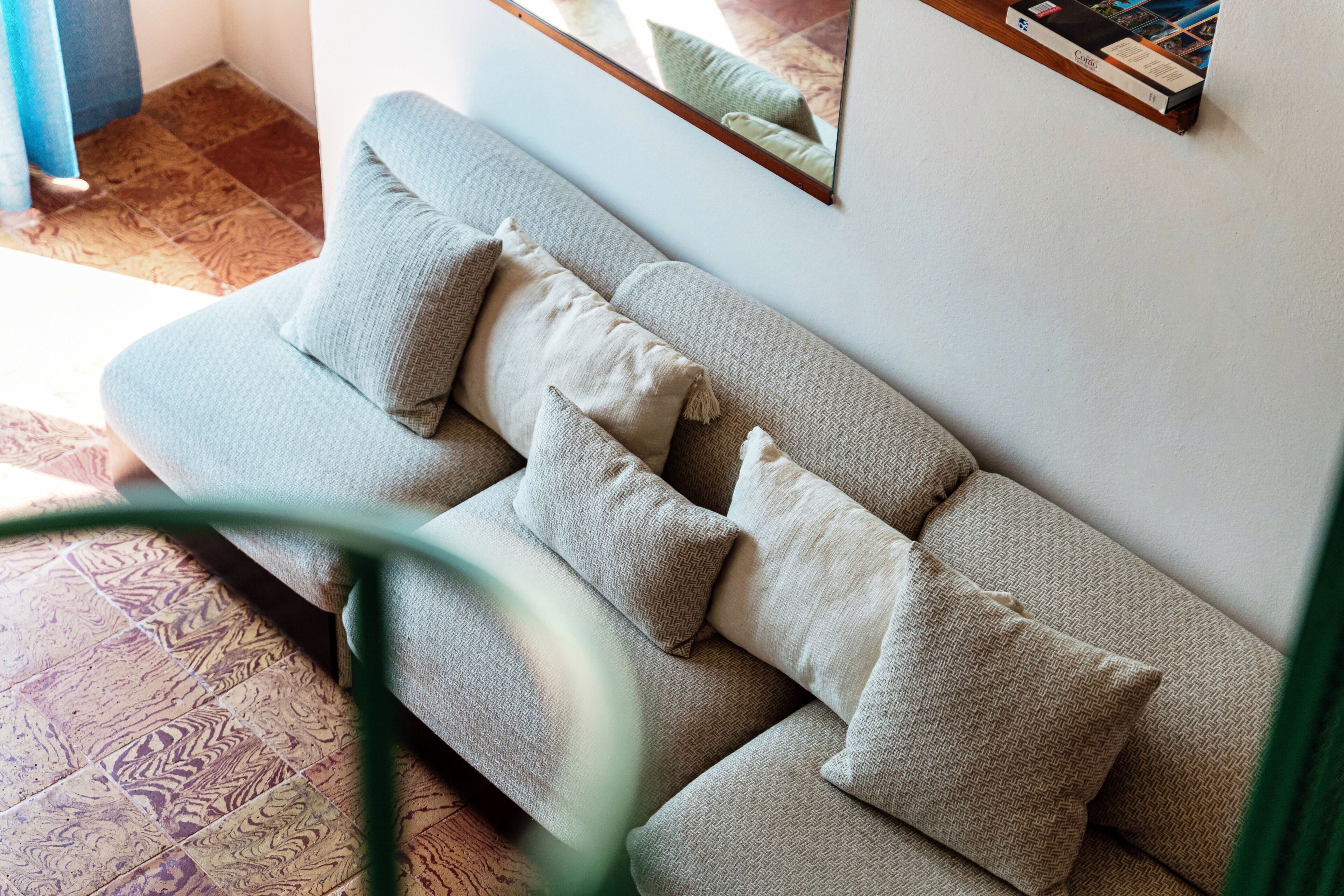 A sofa with multiple cushions, a mirror on the wall, and a patterned floor.