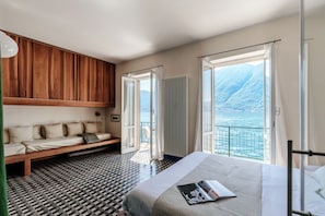Een slaapkamer met een bed, een houten bankje, een vloer met patroon en uitzicht op zee.