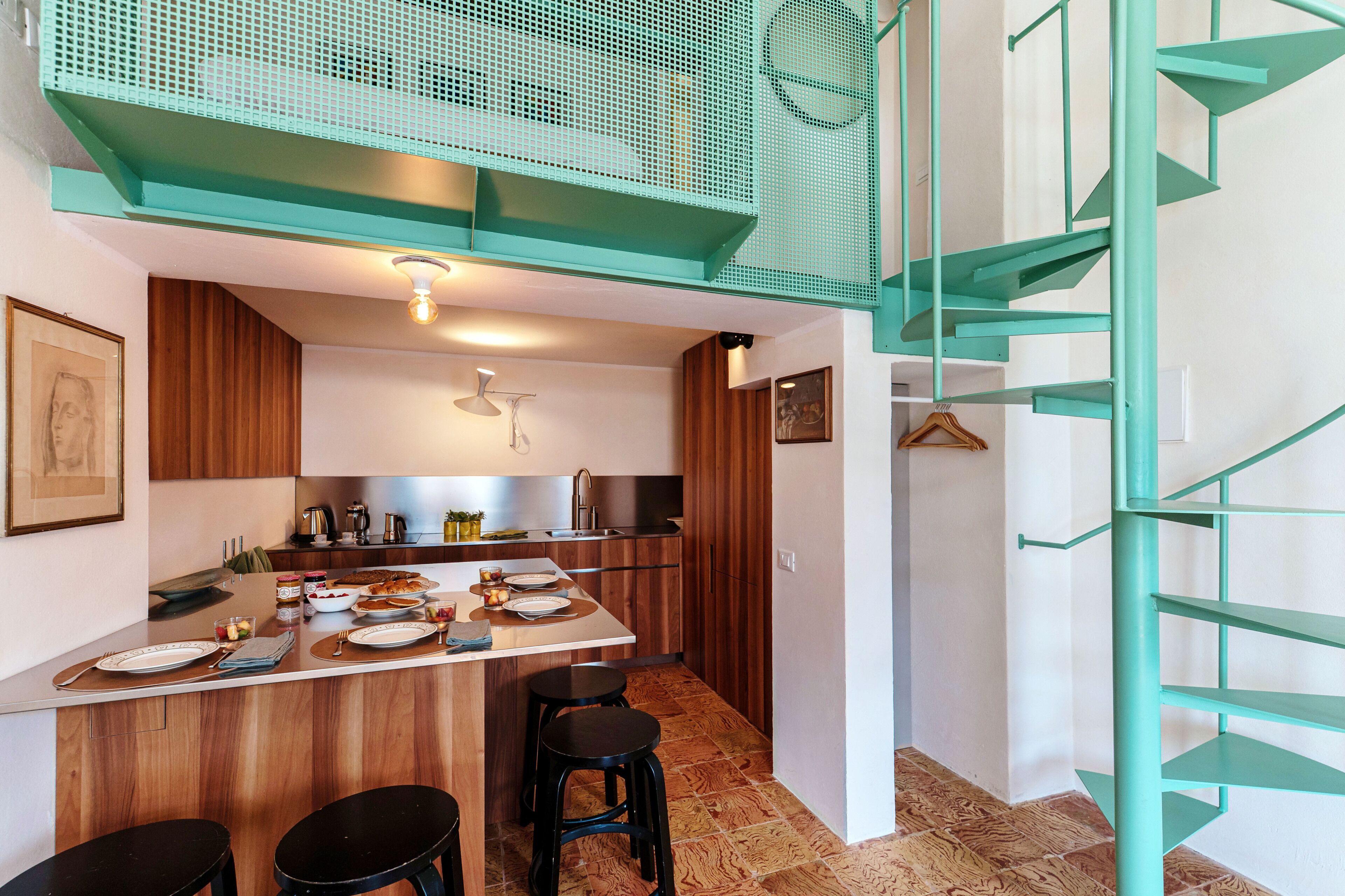 Une cuisine moderne avec des meubles en bois, un îlot central et un escalier en colimaçon de couleur turquoise.