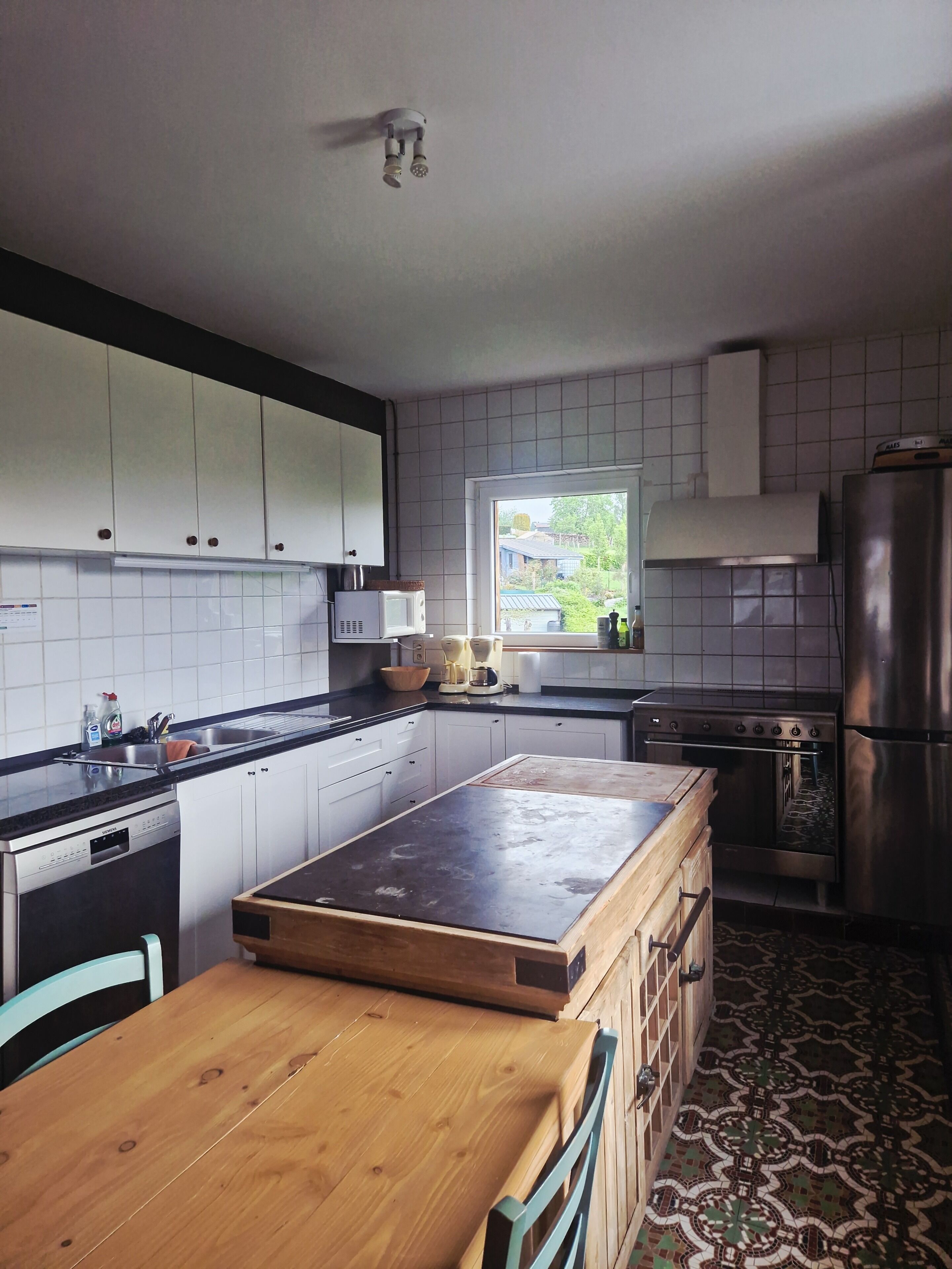 Een keuken met witte kastjes, een houten eiland, een inbouwoven en een raam met uitzicht op groen.