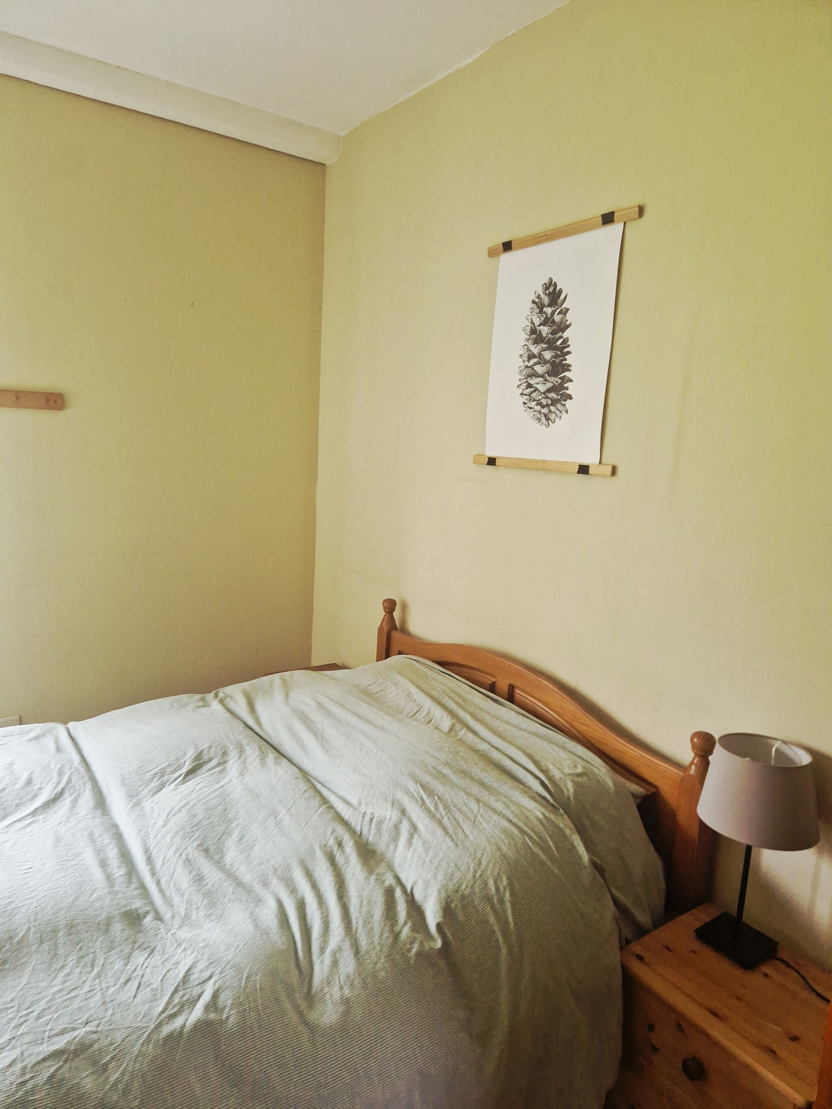 Et soveværelse med en seng, et trænatbord med en lampe og et billede i ramme på væggen.