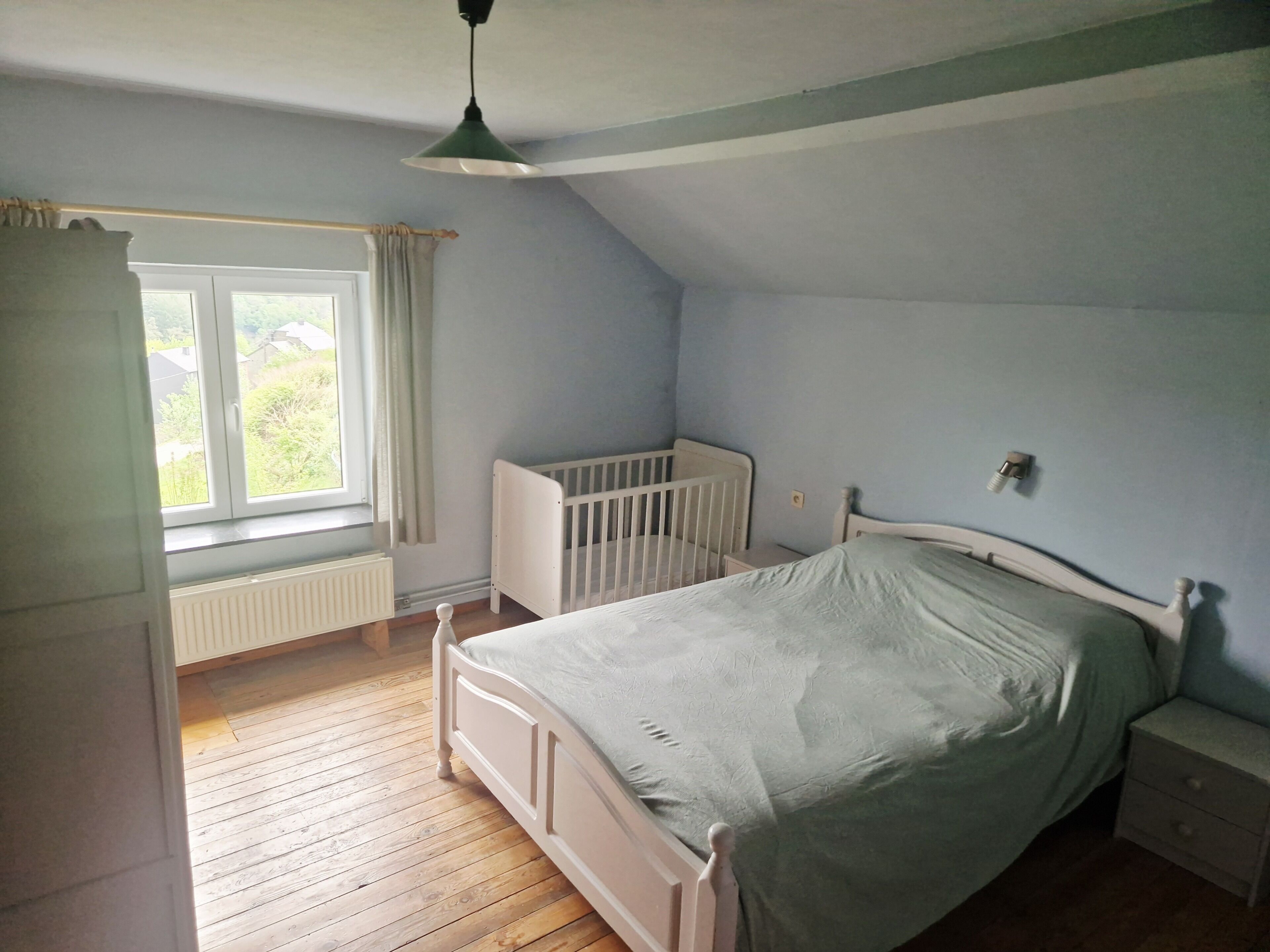 A bedroom with a single bed, a crib, a window with curtains, and a radiator.