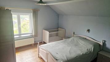 A bedroom with a single bed, a crib, a window with curtains, and a radiator.