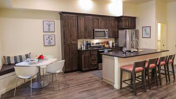 A modern kitchen with dark wood cabinets, stainless steel appliances, a central island with bar stools, and a dining area with white chairs.