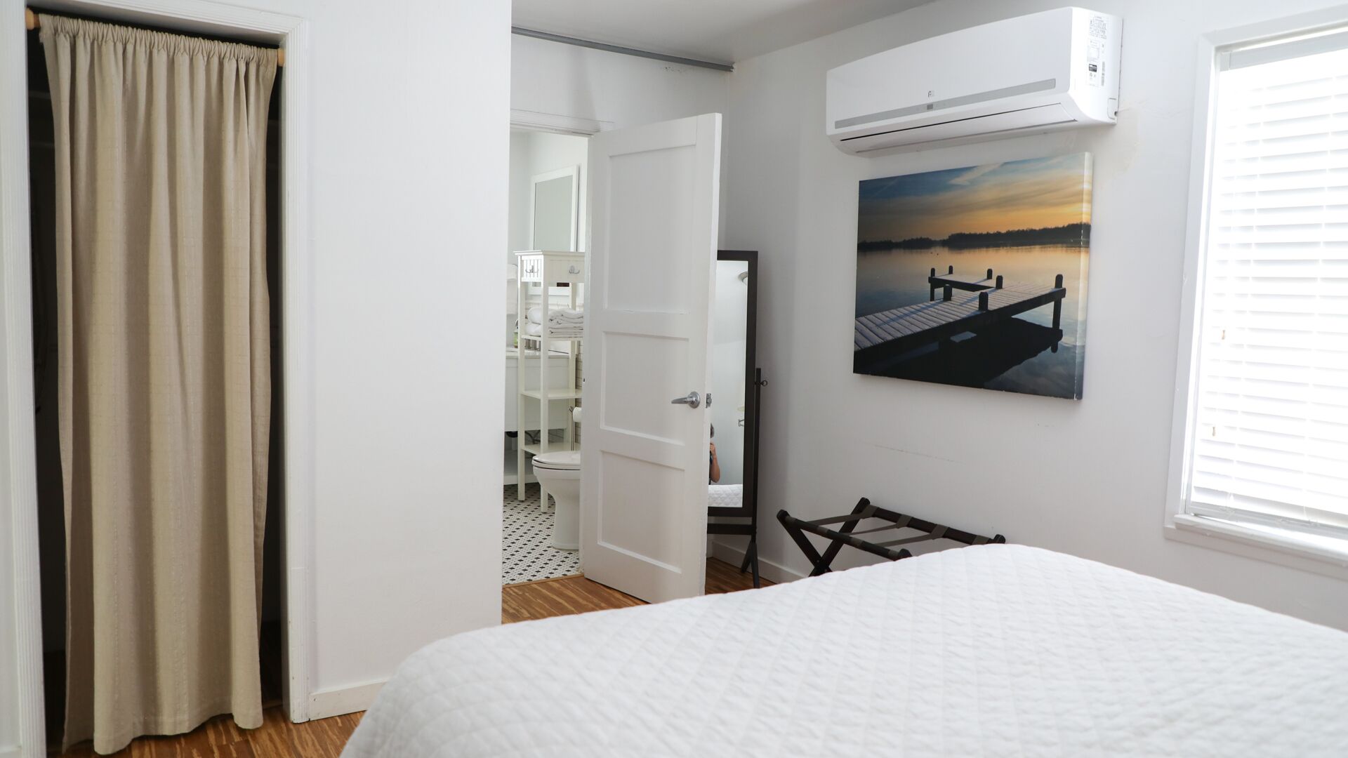 Un dormitorio con una cama, un equipo de aire acondicionado, un cuadro y una puerta que da al baño.
