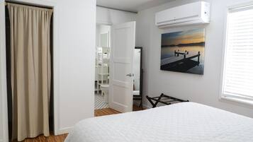 Un dormitorio con una cama, un equipo de aire acondicionado, un cuadro y una puerta que da al baño.