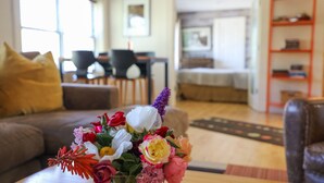 A living room with a sofa, a coffee table with a floral arrangement, a dining area with chairs, and a bed in the background. - Suites On Main (Kelseyville)