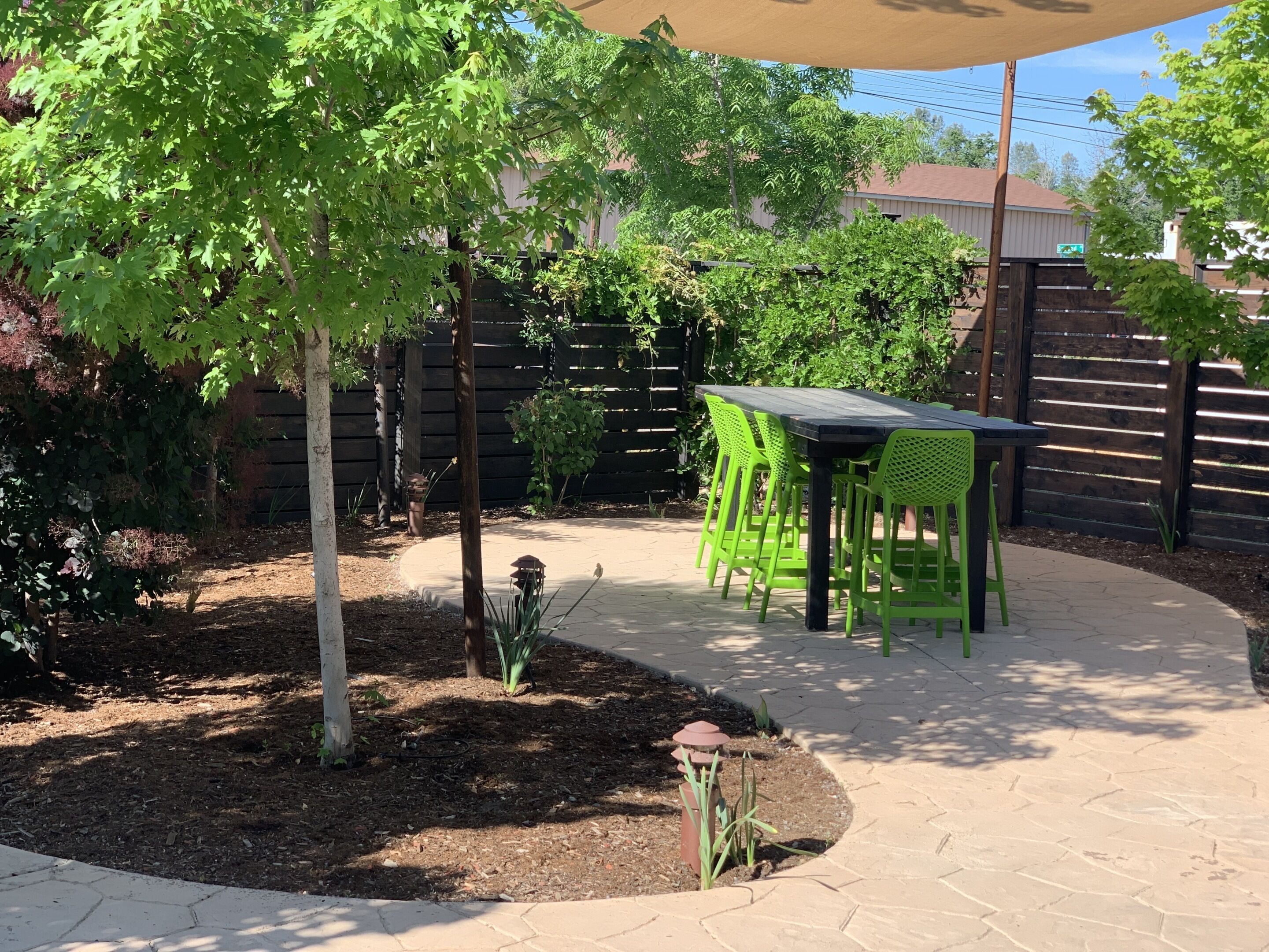Un patio con mesa y sillas, rodeado de árboles y una valla.