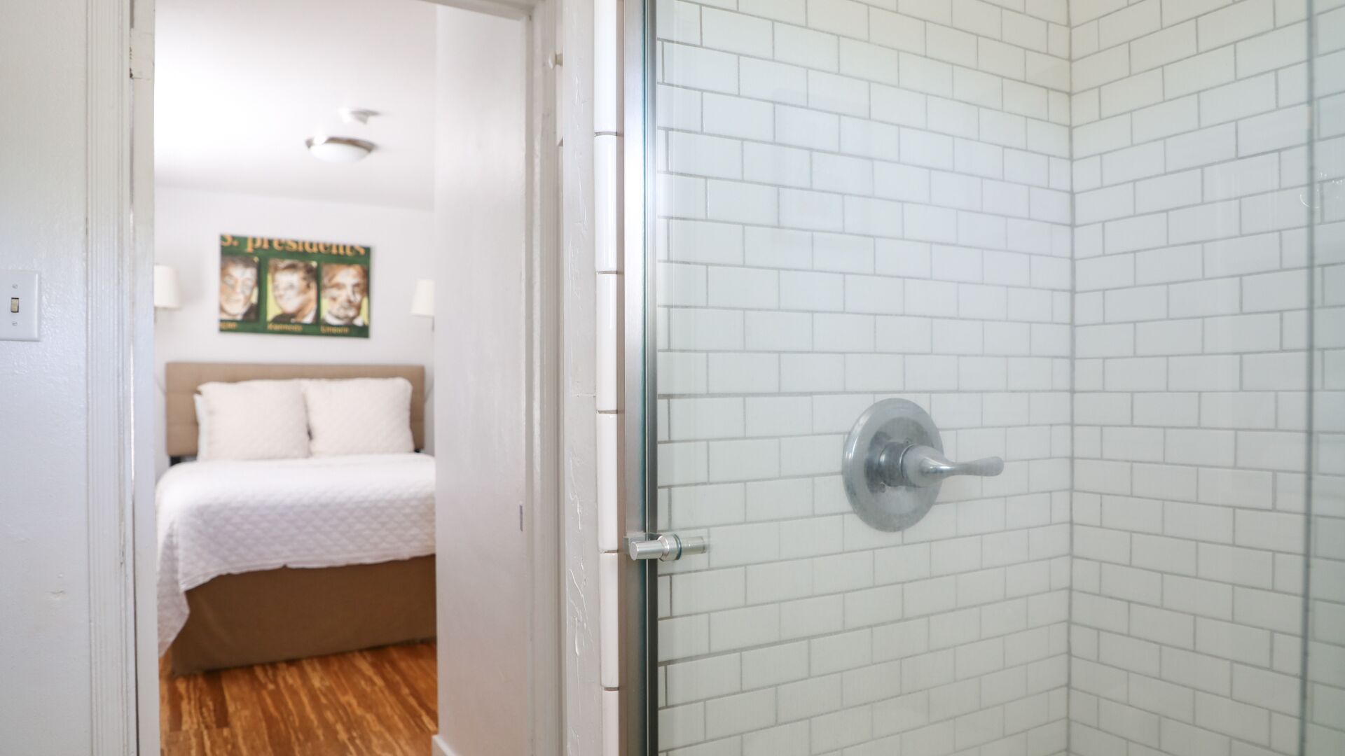 A room with a bed, a shower with white tiles, and a poster on the wall.