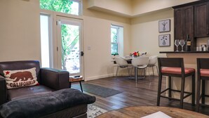 A living room with a leather chair, a dining area with a table and chairs, a kitchen area with bar stools, and a sliding glass door leading to a patio. - Suites On Main (Kelseyville)
