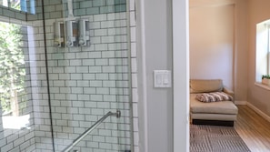 A bathroom with a glass shower enclosure, a towel rack, and a light switch on the wall.
