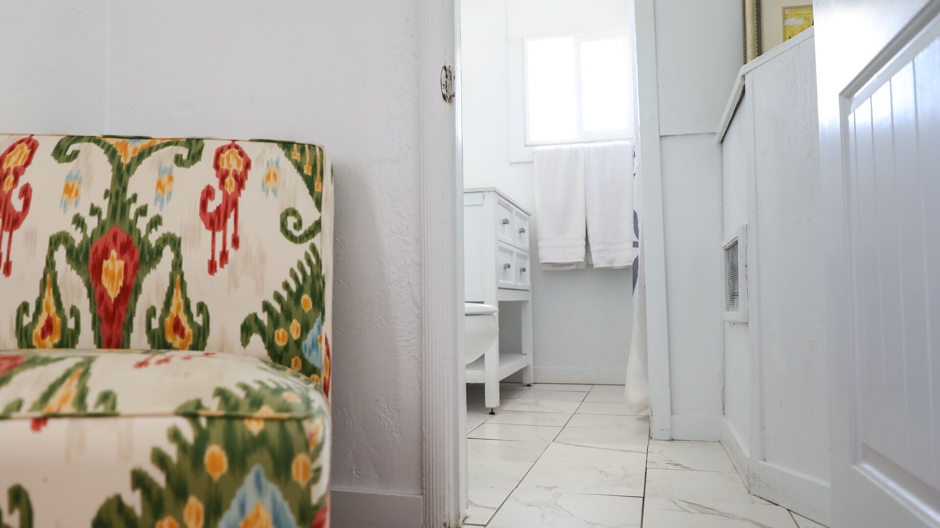 Un pasillo con una silla estampada, un inodoro blanco y un armario blanco.