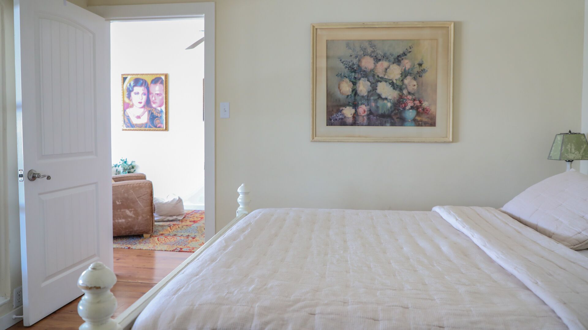 A bedroom with a bed, a door, a painting, and a lamp.