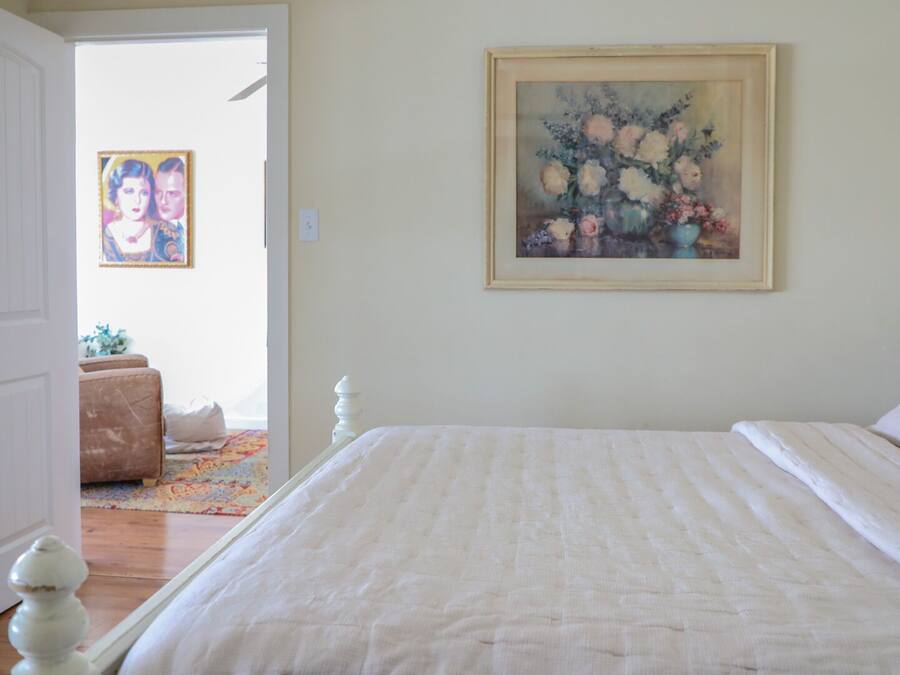 A bedroom with a bed, a door, a painting, and a lamp.