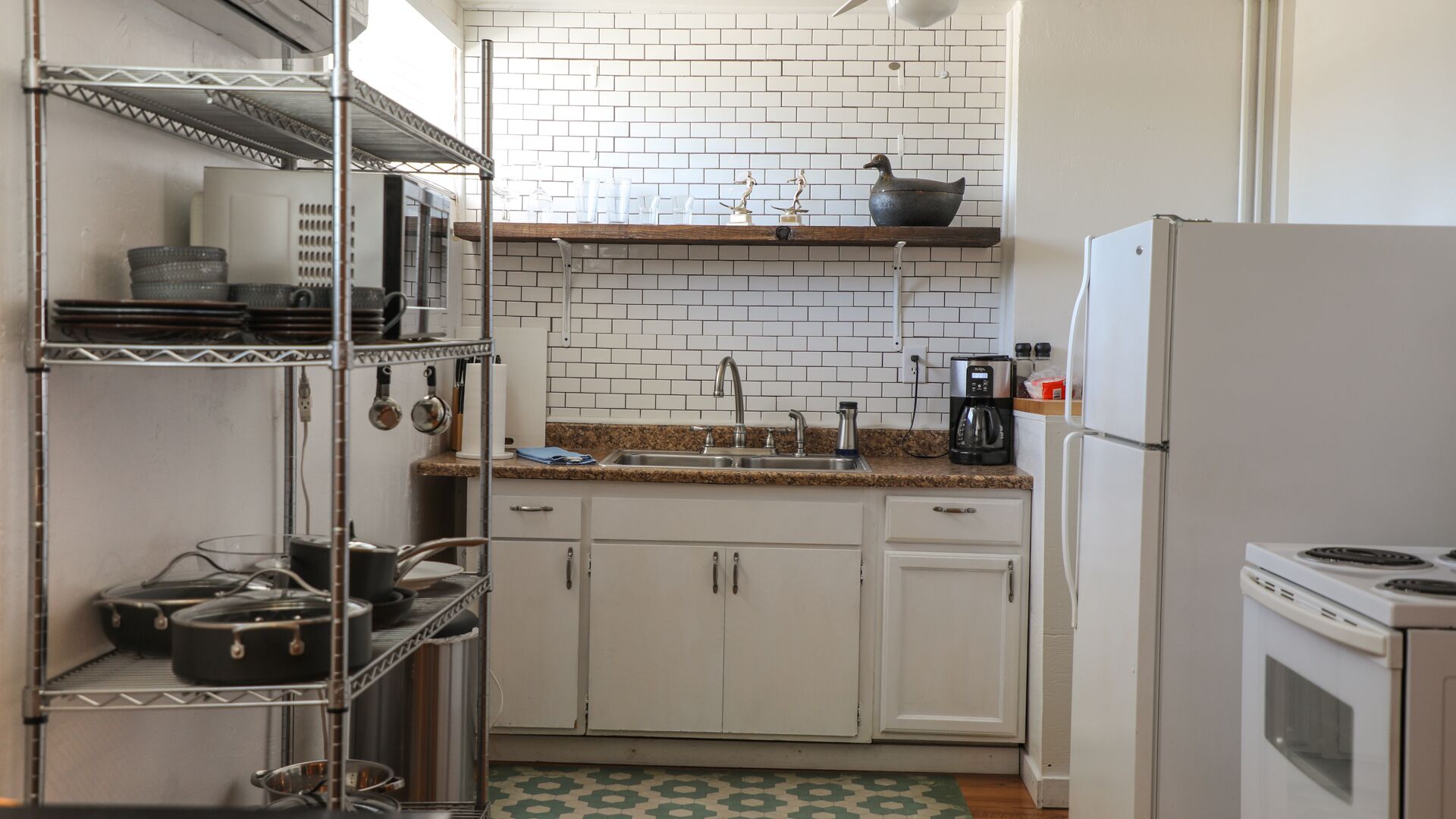 A compact kitchen with white cabinets, a stainless steel sink, a coffee maker, and a refrigerator.