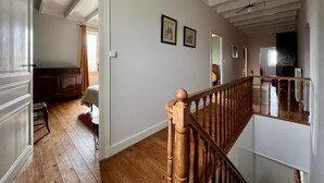 A spacious room with wooden flooring, a staircase with a wooden railing, and a view of a dining area. - 3* family house, sleeps 9, ideal for a quiet vacation with family and friends (Rouffignac)