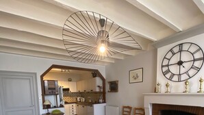 A dining area with a wooden table and chairs, a large wall clock, a fireplace, and a kitchen visible through an archway. - 3* family house, sleeps 9, ideal for a quiet vacation with family and friends (Rouffignac)