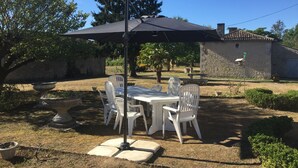 An outdoor patio with a table and chairs, a large umbrella, and a stone wall in the background. - 3* family house, sleeps 9, ideal for a quiet vacation with family and friends (Rouffignac)