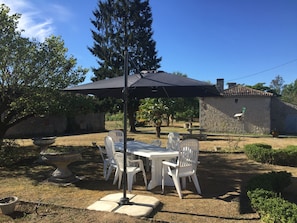Eine Terrasse im Freien mit Tisch und Stühlen, einem großen Sonnenschirm und einer Steinmauer im Hintergrund.