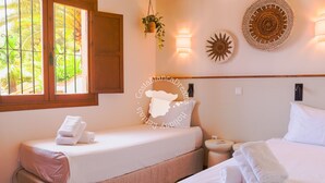 Habitación de hotel con dos camas, una ventana con vista a palmeras, una lámpara de pared y un adorno en la pared.