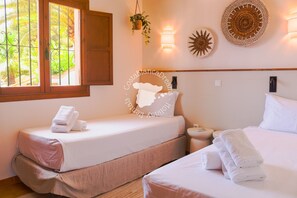 A hotel room with two beds, a window with a view of palm trees, a wall-mounted lamp, and a decorative wall piece. - CostaBlancaDreams - Villa Orquidia in Benissa (Benissa)