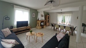 Ein Wohnzimmer mit Sofa, Fernseher, Holzschrank, Esstisch, Stühlen und Deckenventilator.