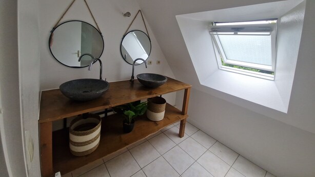 Ein Badezimmer mit zwei runden Spiegeln, einer Holzablage mit Schalen und einem Oberlicht.