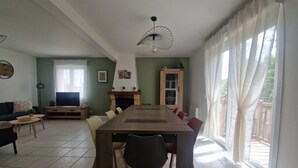 Ein Essbereich mit einem langen Tisch, Stühlen, einem Kamin und Blick ins Freie.