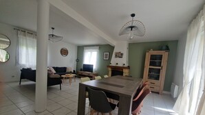 Ein geräumiger Wohnbereich mit Esstisch, Stühlen, einer Couch, einem Fernseher und einem Kamin.